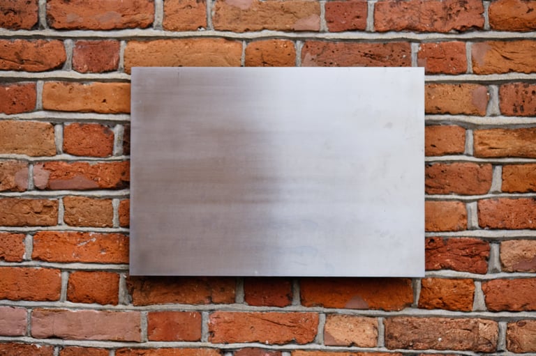 A smooth metal panel is affixed to an old brick wall, showcasing the contrast between the shiny surface and the rough, textured bricks